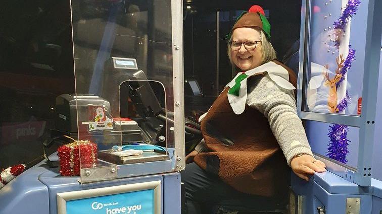 Julie behind the wheel, dressed as a Christmas pudding. She has tinsel around the cab