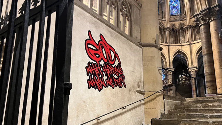 Red graffiti-style writing is on an ancient stone church wall.