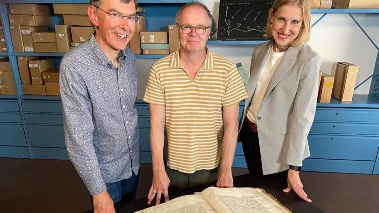 Tim Thornton, wearing a blue shirt, jeans and glasses, stands with actor Jason Watkins, in a yellow striped top and glasses, and presenter and historian Tracey Borman, wearing a grey blazer and with blonde hair.