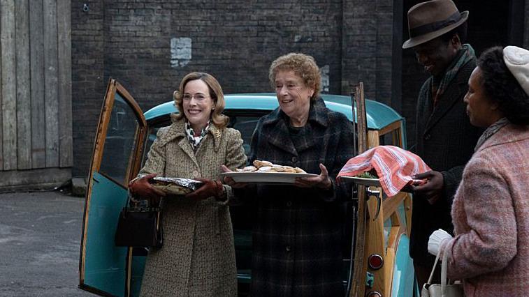 woman and woman hold two plates outside an old van