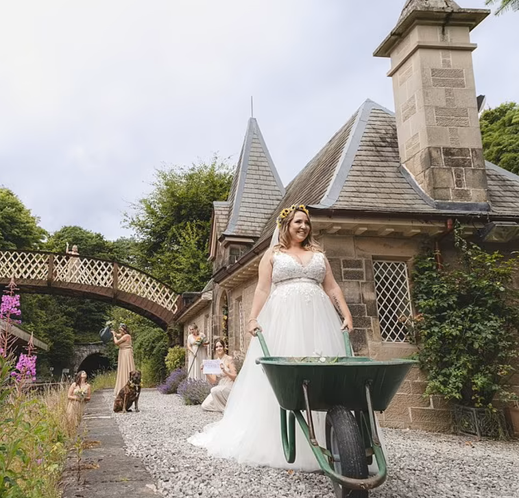 A woman in a wedding dress pushing a wheelbarrow at a heritage rail station