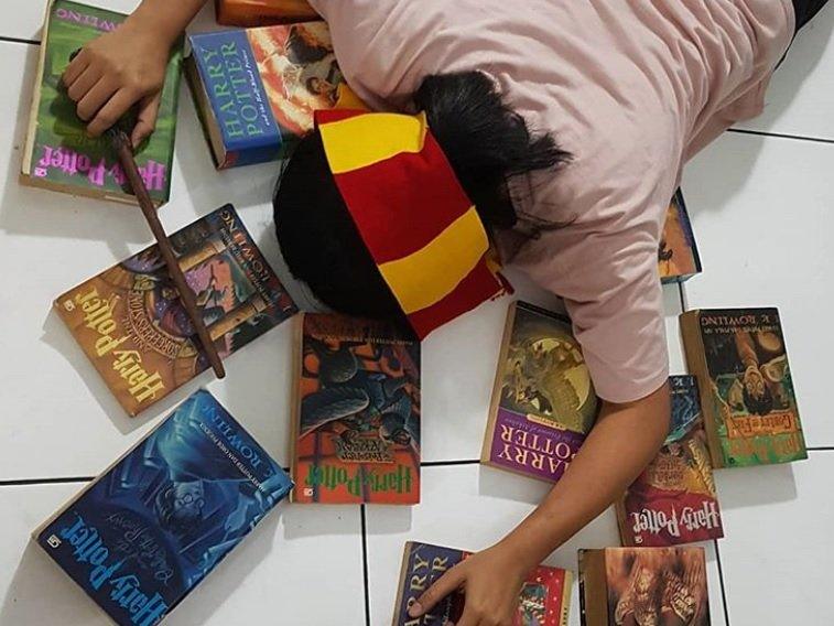 A harry potter fan face down on the floor wearing a hogwarts scarf and surrounded by the books from the series.