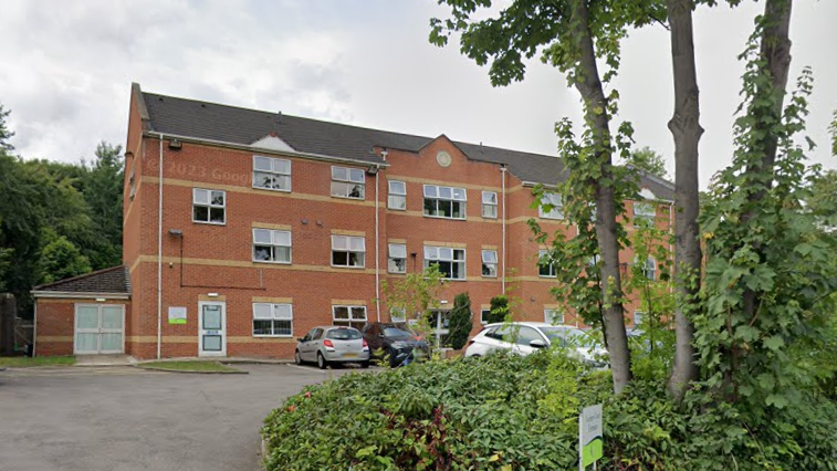 A pale brick building with a car park