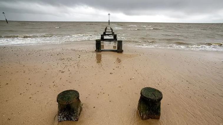 A grey day on Jaywick beach, with wooden stumps and groynes on the sands and out into the sea.