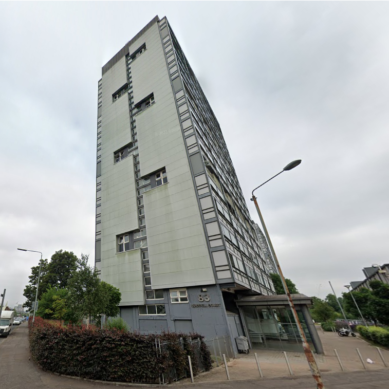 Waddell Court, a large grey multi-storey block rises into the sky, with a sign showing number 83 and "Waddell Court" on the side on the bottom floor.