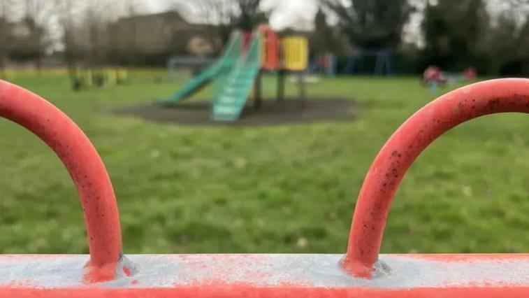 A playground with red round grills and a green slide in the background 