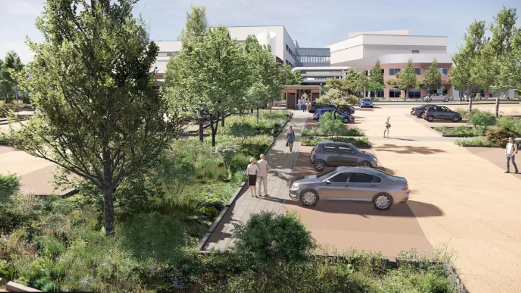 A concept design of the new Acute Hospital at Overdale. On the left there is green trees and plants and a parking area with concept cars. There are people walking down a light grey pavement and the road on the right is light brown. In the distance is the concept designs of the building which is red brick at the bottom and white at the top. 