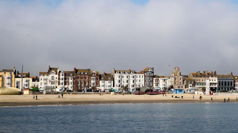 People walk on the beach as sea mist rolls in from the sea at Weymouth as the resort prepares for the start of the holiday season in Dorset, England.