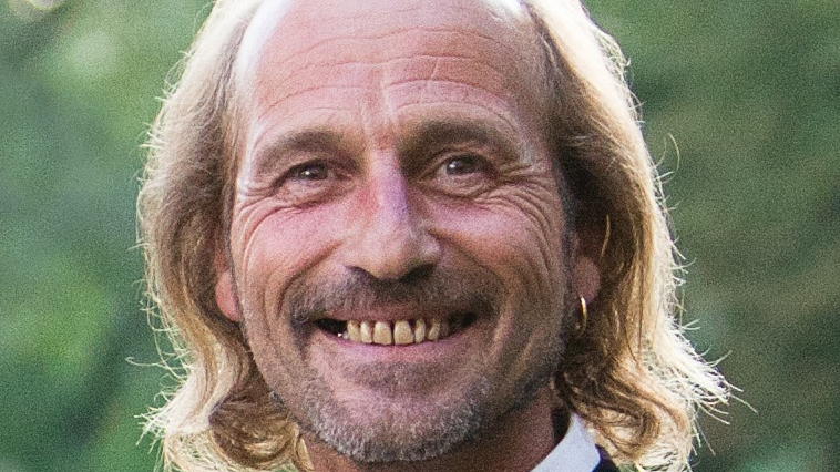 Photo of Dean McCormack smiling. He has neck-length blond hair and a gold hoop earring in one ear.