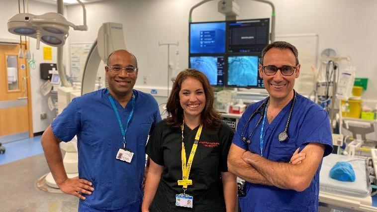 Two male doctors wearing blue scrubs stand either side of a female resuscitation practitioner. They are in a room full of hi-tech hospital equipment at Lincoln County Hospital