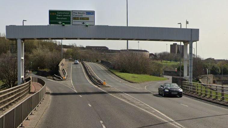 A view of the bridge just before the crash site. There are four lanes, two in each direction, but no barrier between them until halfway up the slope. An overhead gantry signals which lanes go where.