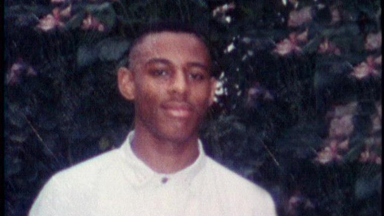 Stephen Lawrence with short black hair wearing a white top