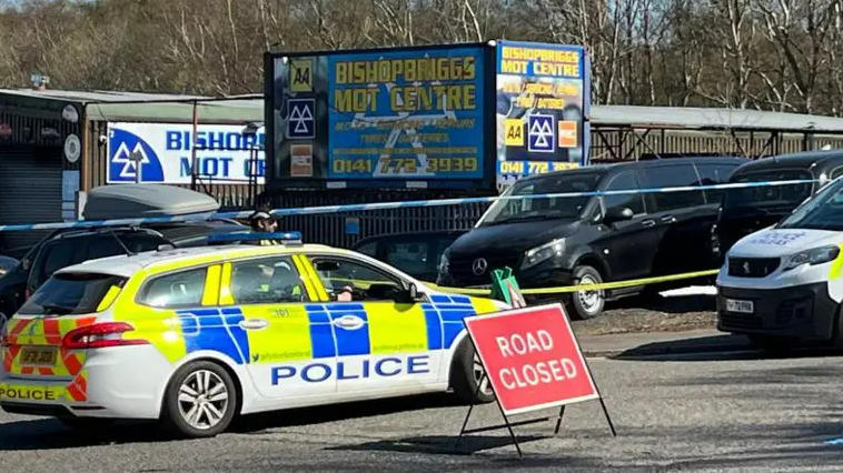 A police car and a road closure sign outside a garage in Bishopbriggs.