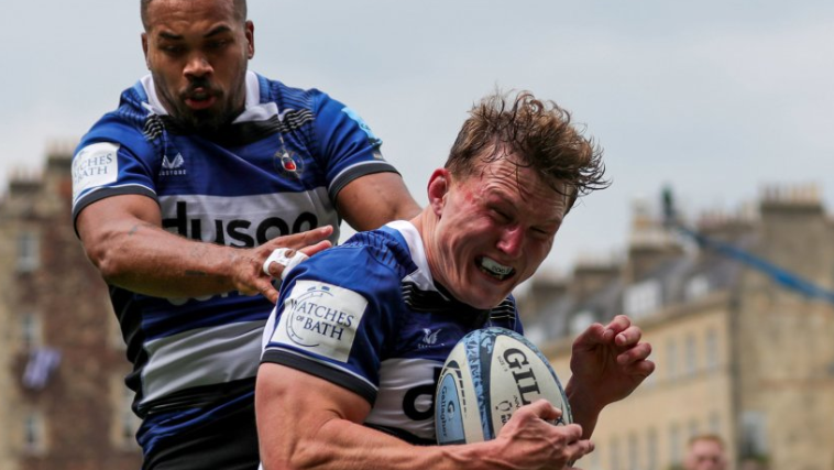 A close-up of Ted Hill scoring a try at the Recreation Ground in Bath gripping the ball with a very tense look on his face and a team player right behind him.