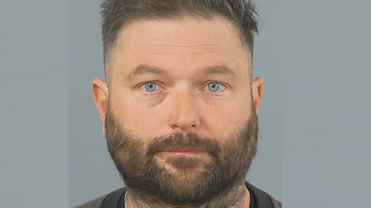 Darren Silvester has a blank expression in a police photo. He has brown hair, closely shaved at the sides, and a beard.