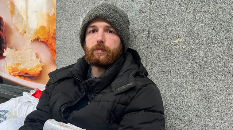 A homeless man sat in front of a shop 