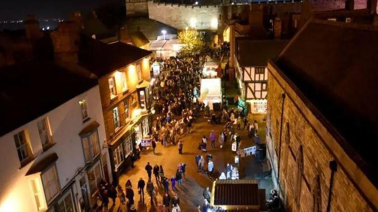 A night-time shot showing hoards of people at a previous Lincoln Christmas Market. In the distance is the illuminated Lincoln Castle  