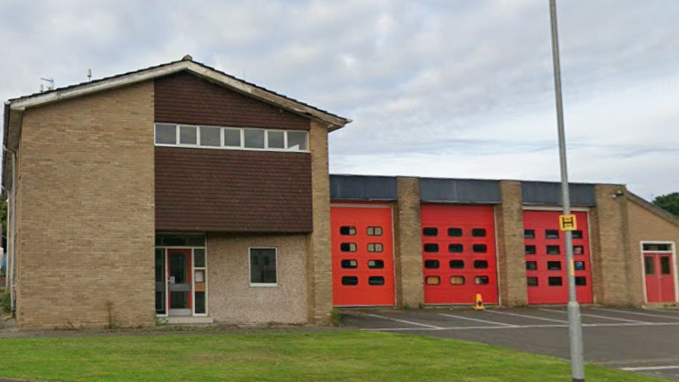 Hexham's former fire station. It is a two-storey brick building with an appendage to the right, with three large doors, presumably for fire engines to enter and leave via. There is a lawn to the front of it.