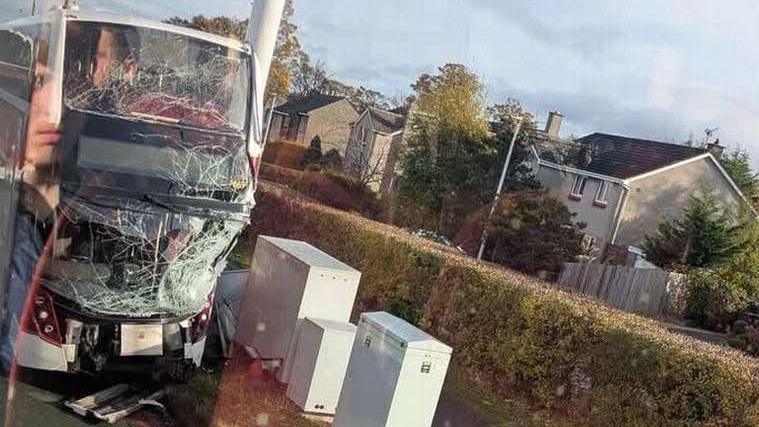 Image of a double decker bus with a shattered front windscreen and top deck window. Houses can be seen in the background.