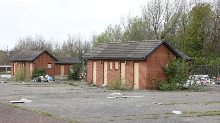 Two brick buildings on land and rubbish in background