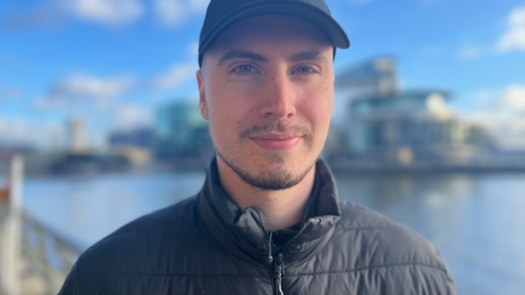 Kyle stands outside, next to the canal, looking towards the camera