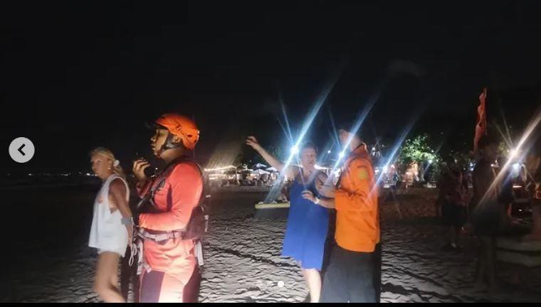 A member of search and rescue wears an orange helmet on a beach. It is dark and he is with three other people