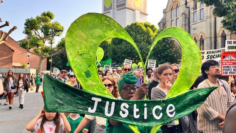 Grenfell campaigners carrying placards and signs march through west London