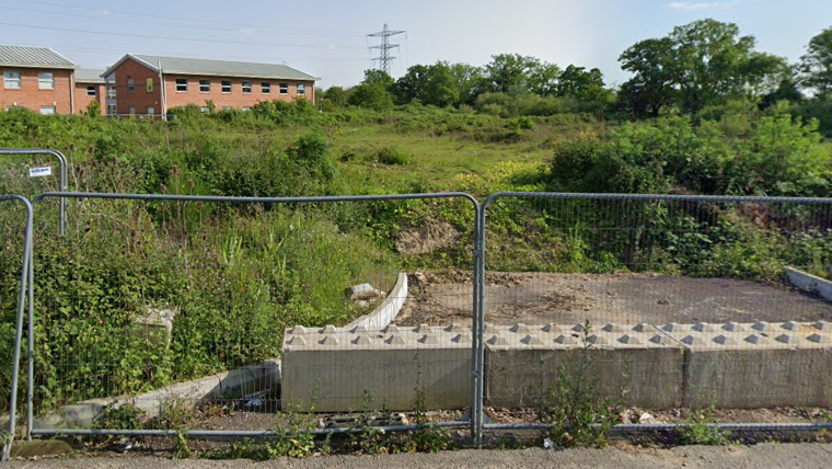 Shrubs and grass cover wasteland behind panels of wire fencing