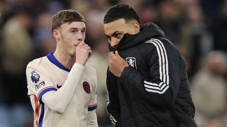 Cole Palmer and Morgan Rogers hiding their mouths while speaking to each other after a match