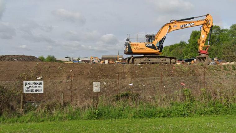 A yellow Penman digger behind a fence on the former James Penman Plant Hire site in Kirkcaldy.