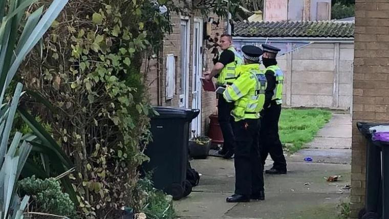 Three police officers standing outside a side door at the property in Fold Hill, Friskney, near Skegness