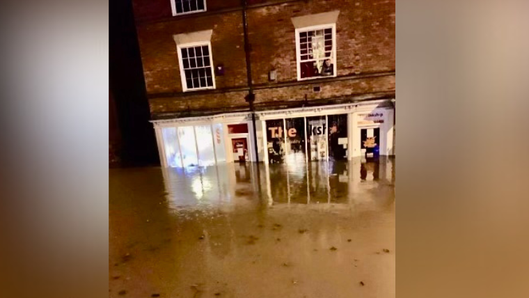 Dirty flood water swamping a high street with water pictured half way up the front of the windows of two shops