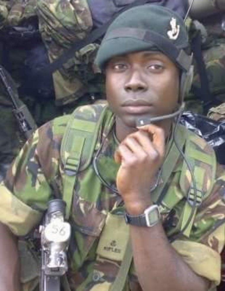 OB wears a green military camouflage kit, and a beret with The Rifles badge on it. He is holding  mouthpiece. 