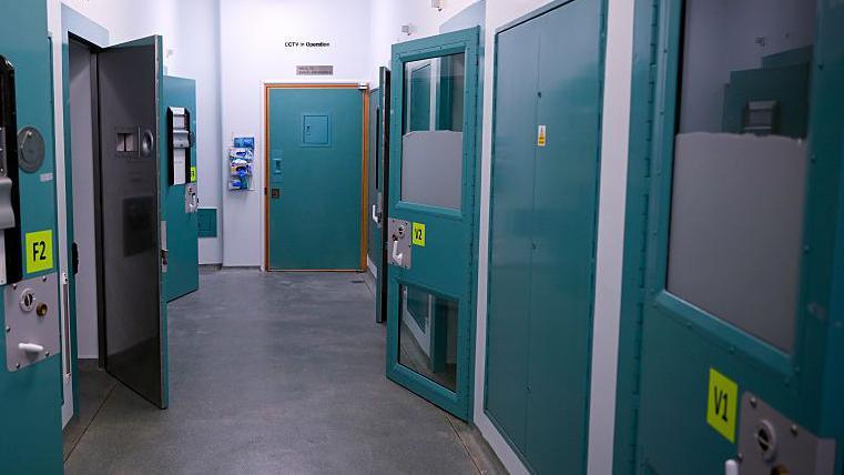 A police custody suite. A corridor with high security doors on either side.