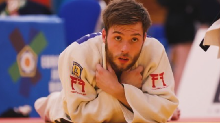 Rowan Kinsella in judo kit lying propped up on his elbows in a judo arena 