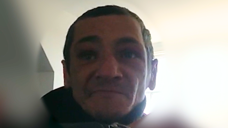 Ciprian Ilie as seen via a police bodyworn camera. He has short dark hair and stubble. He is looking slightly resigned as he gets arrested. The background is blurred.