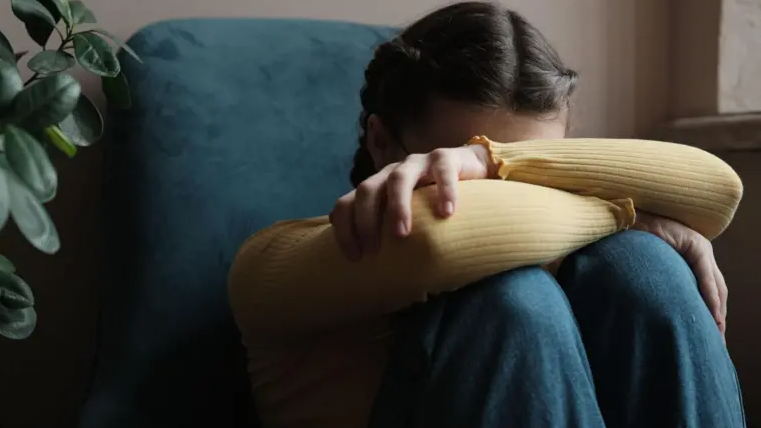 A stock image of a potential domestic abuse victim sat on the floor with her knees up and arms folded across her knees. Her head is leaning on her left arm. 