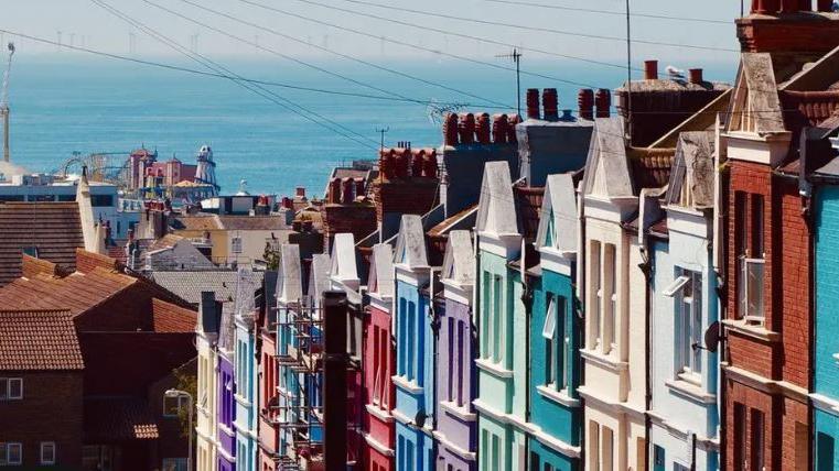 An aerial shot of multi-coloured houses with the sea and amusements on Brighton Pier in the background