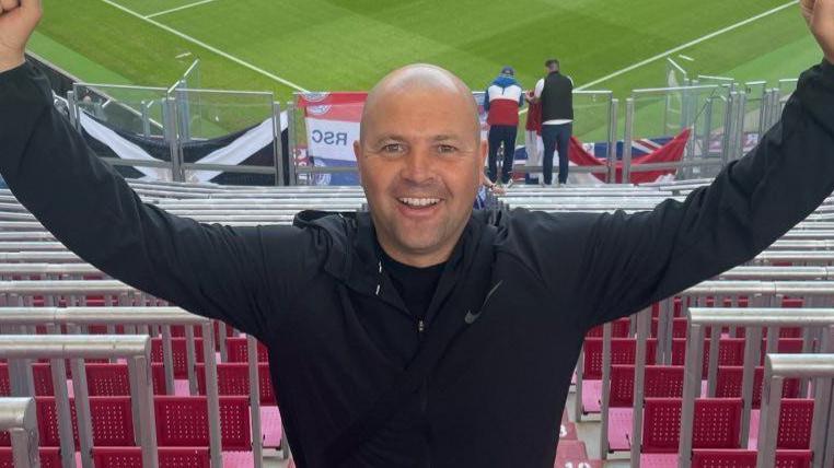 Christopher Potter with his arms raised at ibrox stadium in front of the seats in the stand