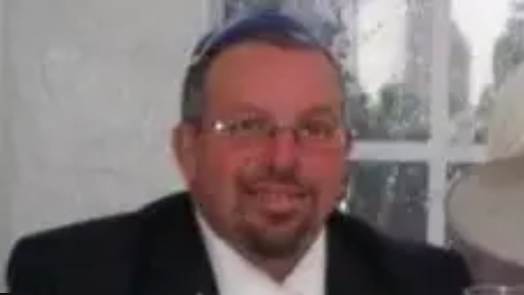 A pixelated photo of Melvin Cravits smiling at the camera. He wears glasses and has a moustache and a trimmed beard.
