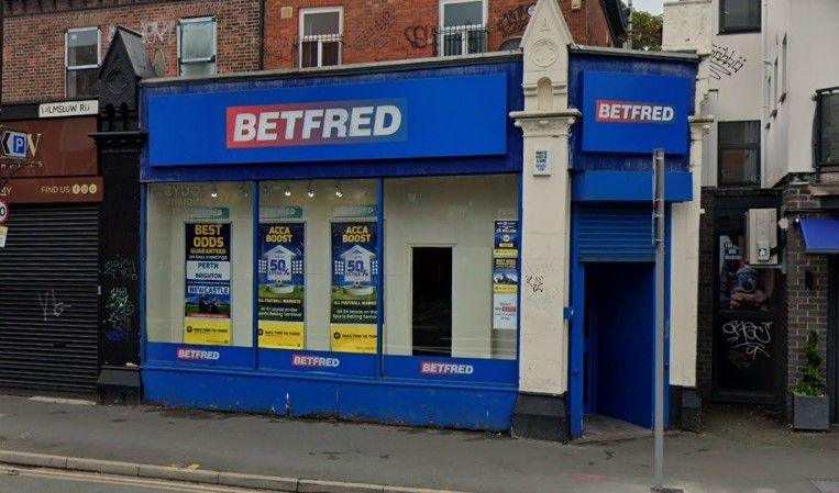 A blue-fronted BetFred shop, with blue shutters partially closed over the door and a window filled with adverts for betting offers