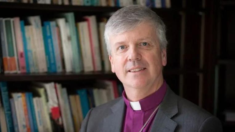 Close up shot of Andrew Watson, Bishop of Guildford, indoors wearing a dog collar and grey jacket