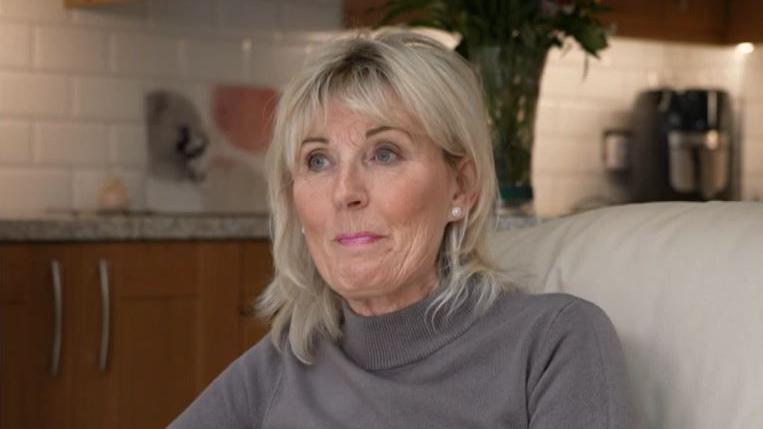 Sue Mountain. She has blonde shoulder length hair and is wearing a grey top.