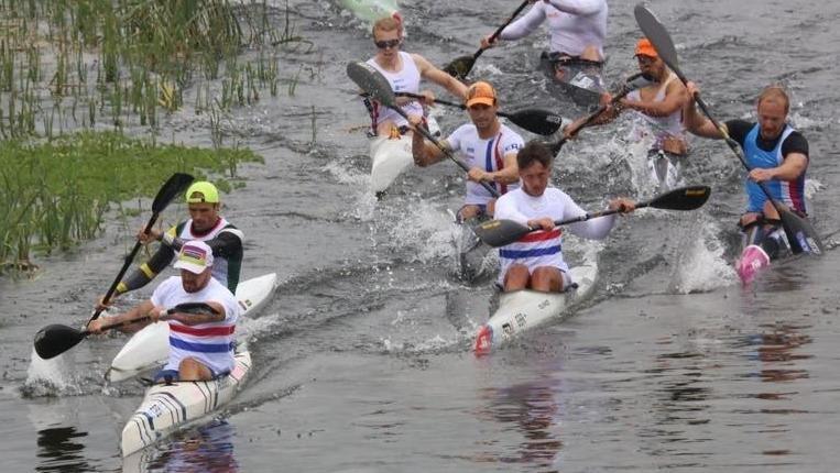 Men in canoes on a river competing in a race. They are paddling fast and are close together.
