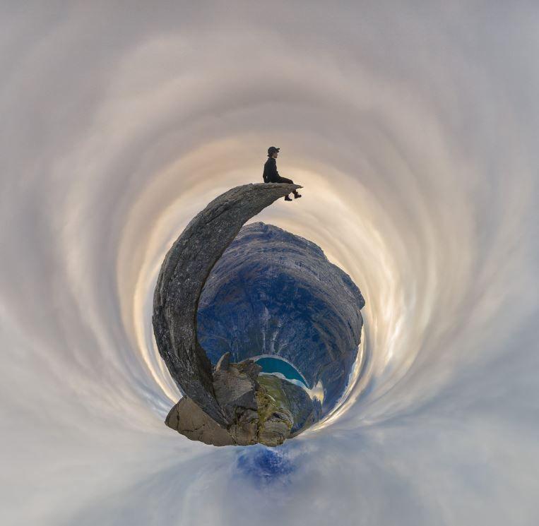 fish eye image of a figure sitting on a cliff edge