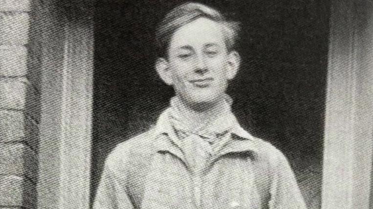 Martin Boysen, pictured as a teenager, is standing in the doorway of a home. He is smiling directly at the camera in this black and white image. 