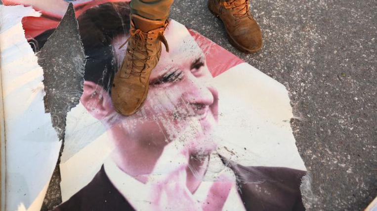 A pair of battered boots can be seen standing on a torn and dirty poster of Syrian President Assad. 