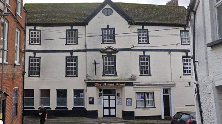 A large three story white building with a dark sign saying The Kings Arms above a black and white door