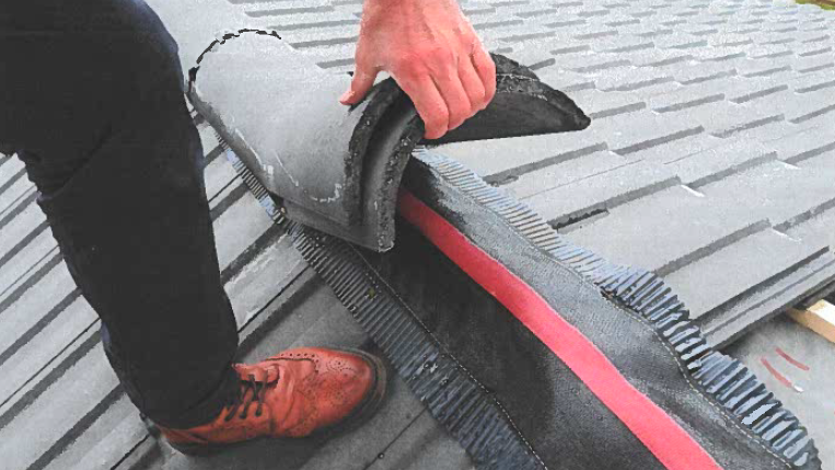 A building inspector lifting up a tile on a roof ridge