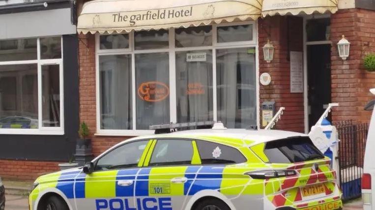 A marked police vehicle parked in front of a red bricked terraced building, the entrance to the Garfield Hotel